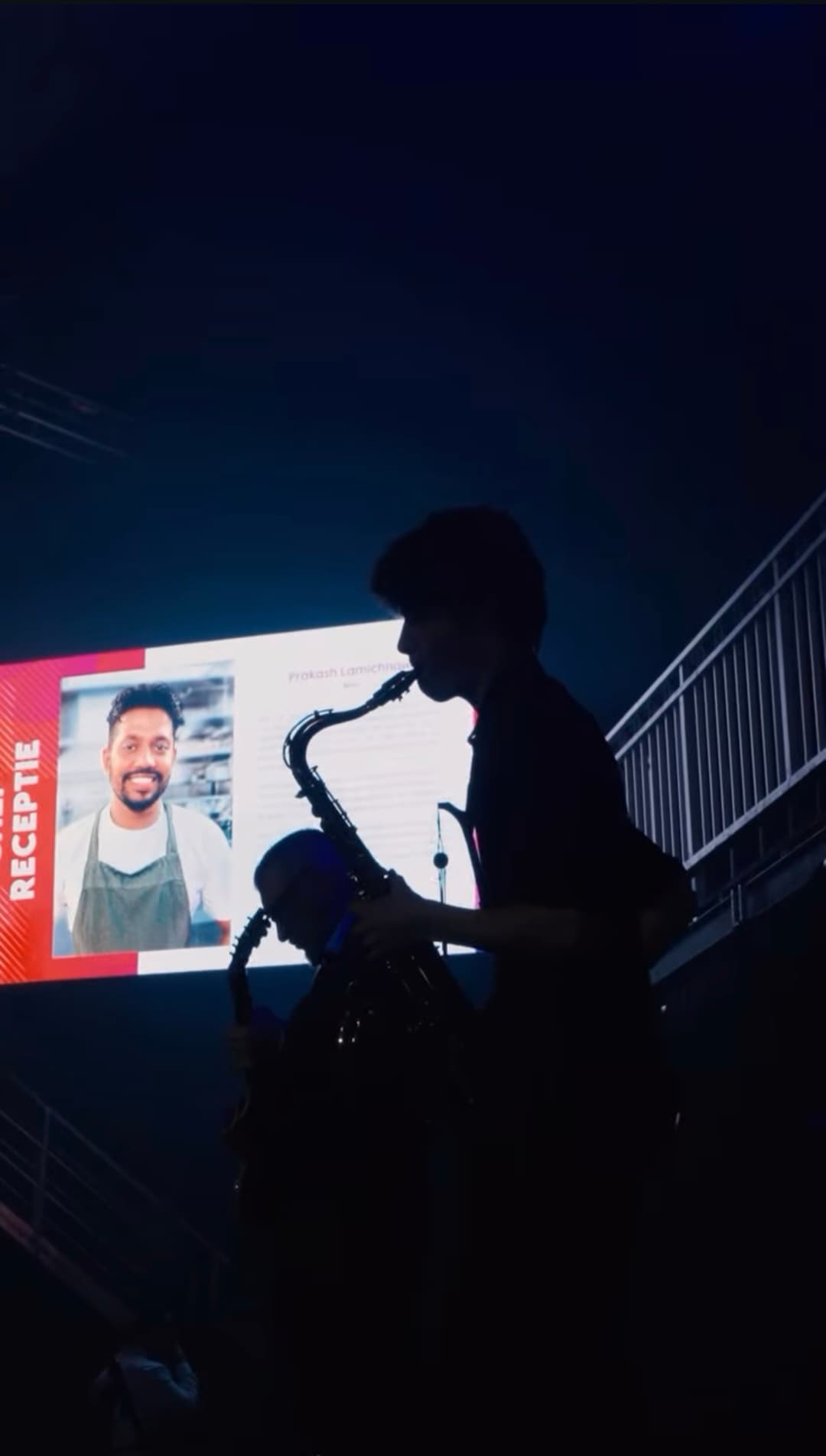 Silhouette of Louis playing saxophone in front of a projection screen at an evening reception